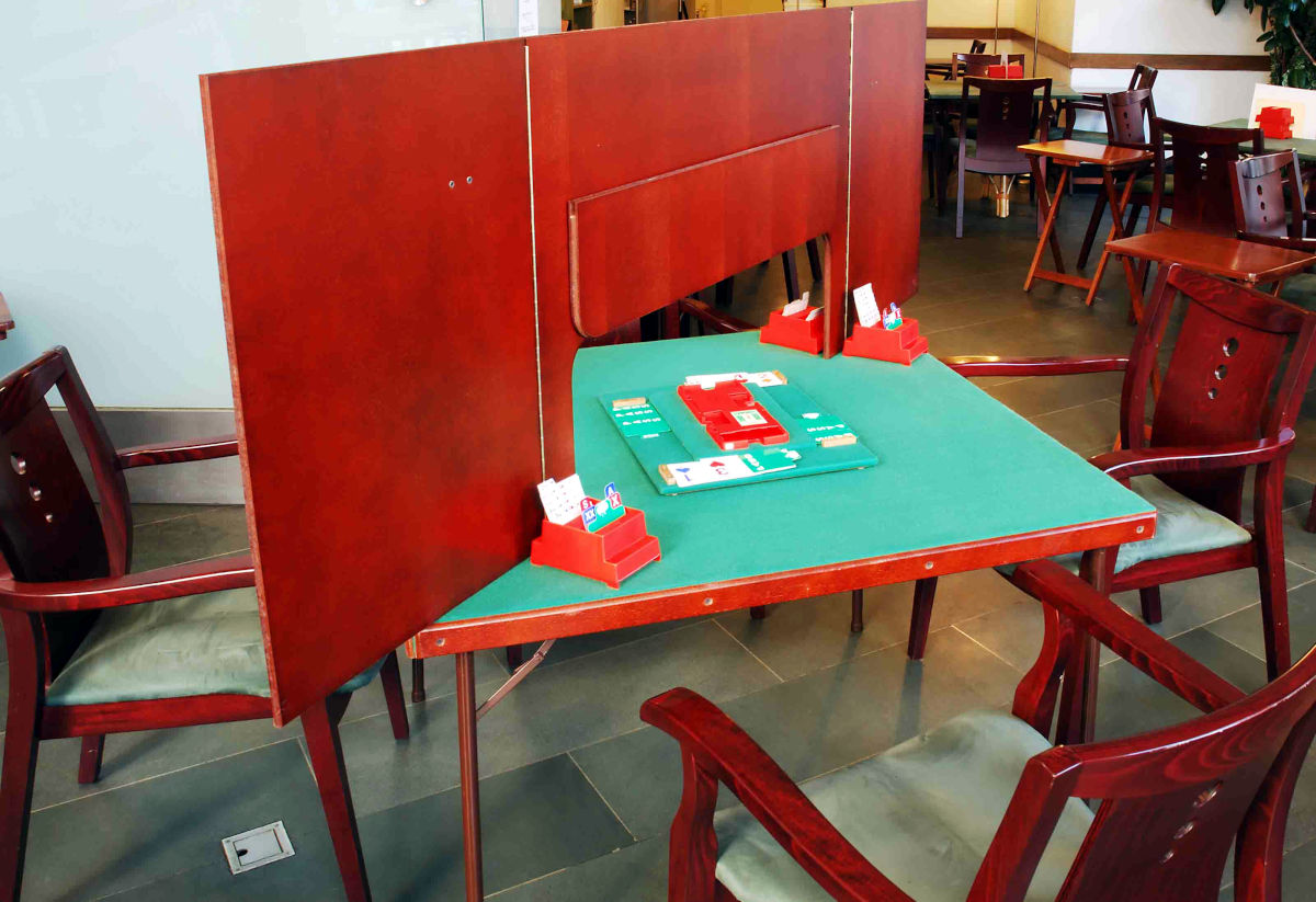 Bridge table with screen (above table), showing bidding boxes and bridge board which provides the pre-prepared card deals for duplicate and tournament bridge